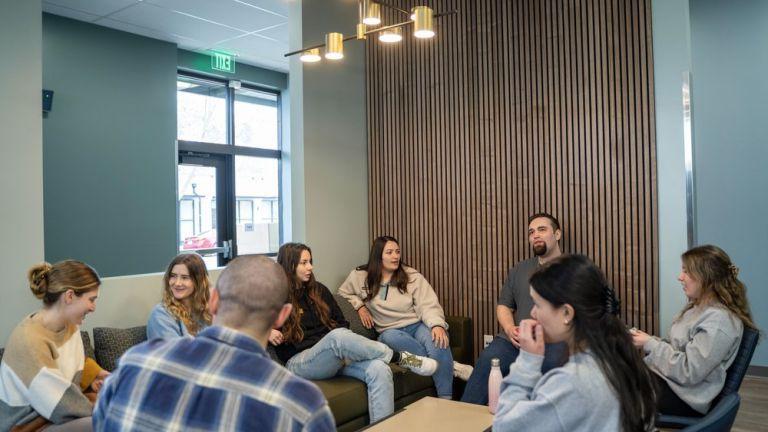 Photo shows a group of students talking while sitting in the student lounge. 